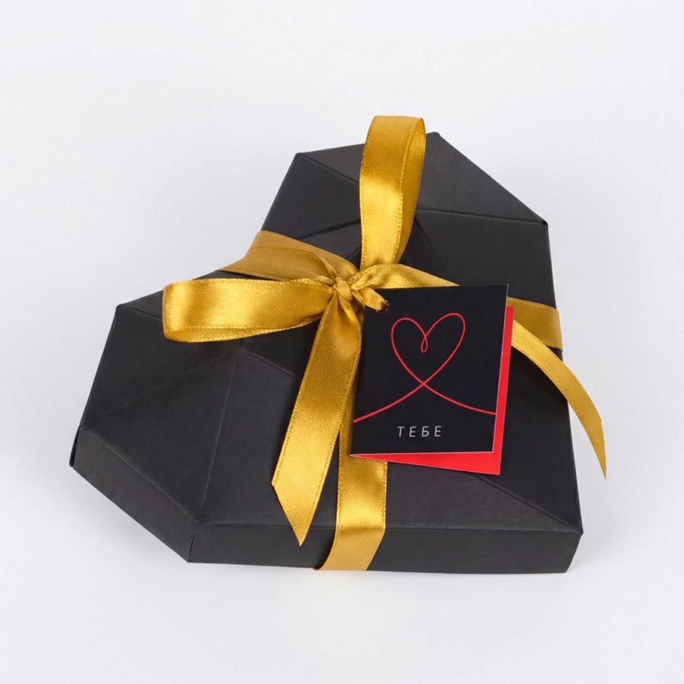 Чёрная коробка-сердце закрытая с золотой лентой и открыткой «Тебе»